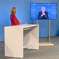 Innenminister Joachim Herrmann digital auf Bildschirm im Studio mit Moderatorin
