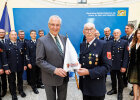 Herrmann und Feuerwehrkommandant mit bedrucktem Schirm, im Hintergrund Feuerwehrleute in Uniform
