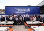 Gruppenfoto mit Kirchner, Geistlichkeiten, Ehrengäste sowie THW-Helfern hinter Festbänken, vor THW-Wand