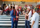 Innenminister Joachim Herrmann in Konversation mit Schulleitern mit Büchern zu Zubza in den Händen, im Hintergrund Schulkinder, alle mit traditionellen Schals geschmückt