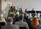 Blick über Publikum Richtung Bühne, dort Herrmann hinter Pult, daneben Musikkapelle
