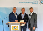Innenminister Joachim Herrmann neben Alexander Brochier mit Bundesverdienstkreuz am Bande und Urkunde, rechts daneben eine weitere Person