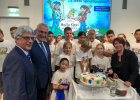 Staatsminister Herrmann neben weiteren Personen sowie Kindern mit einheitlichem T-Shirt stehen um eine bunte Klexitorte herum