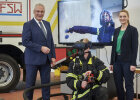 Herrmann und Gerlach neben Feuerwehrmann mit VR-Brille, dahinter Bildschirm mit Übungsszenario
