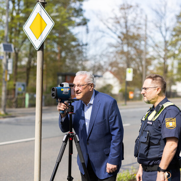 Herrmann blickt durch Messgerät, neben ihm ein Polizist