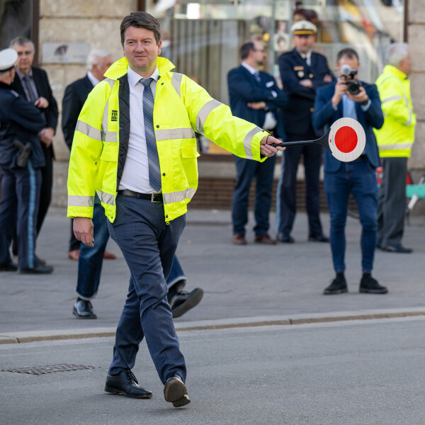 Kirchner mit Schülerlotsenkelle und gelber Warnweste geht über die Straße