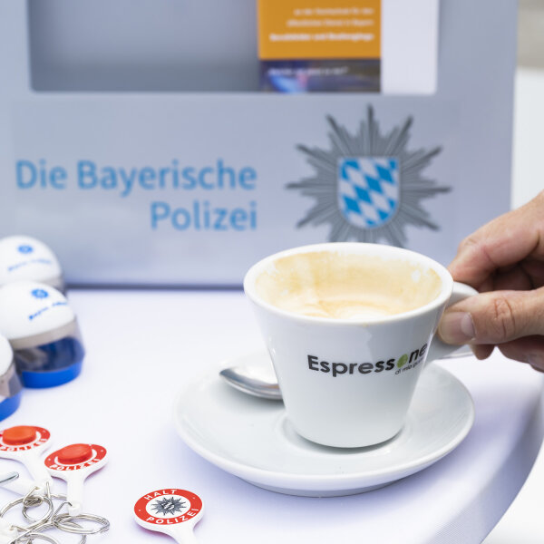 Hand greift Espressotasse auf Tisch mit Polizei-Giveaways und Polizeilogo