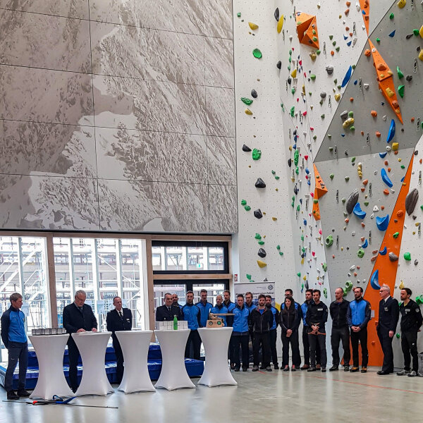 Herrmann und Weitere an Stehtischen, rechts Bergführer/innen vor Kletterwand