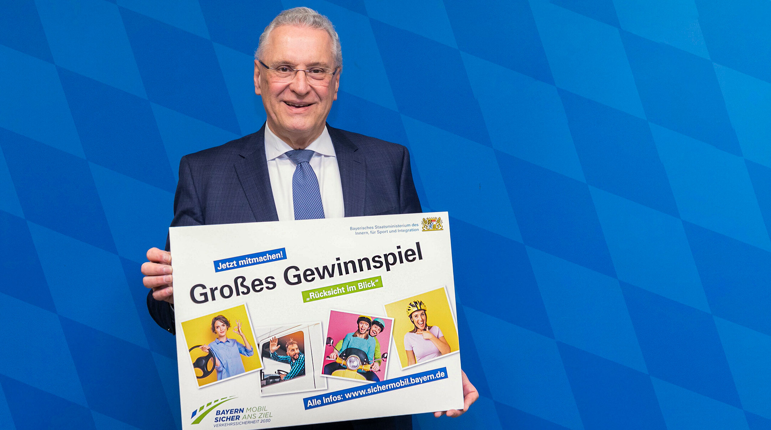 Innenminister Joachim Herrmann hält Schild "Großes Gewinnspiel - Jetzt mitmachen"