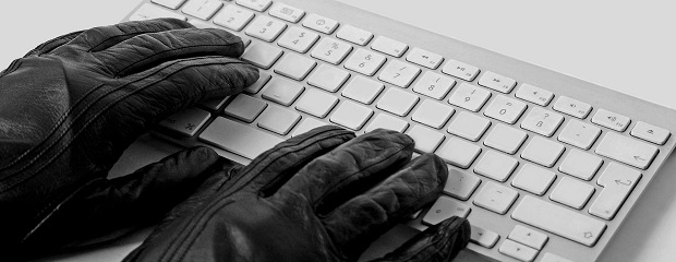 Das Foto zeigt zwei Hände in schwarzen Lederhandschuhen die auf einer Computertastatur liegen.